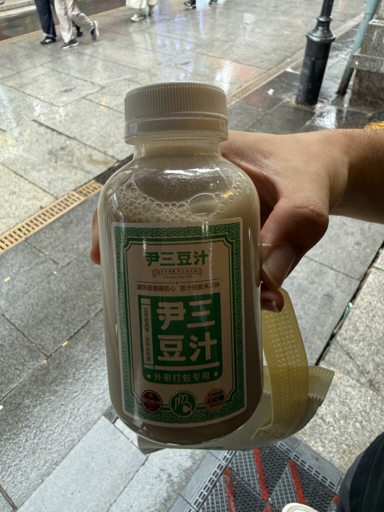 雨天的北京街头，手里拿着一瓶豆汁。